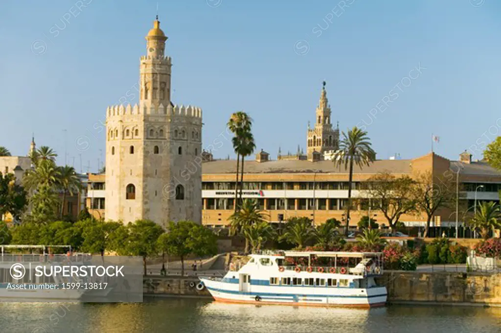 View of the tour boats and octagonal tower of Torre del Oro makes golden reflection on Canal de Alfonso of Rio Guadalquivir River, Sevilla Spain