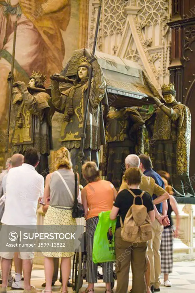 Tourists look at the mausoleum-monument and ornate tomb of Christopher Columbus where four heralds dressed in full court mourning carry the sarcophagus; they bear respectively the arms of, Castile, Léon, Aragon, and Navarre, the four nations which united under the rule of Ferdinand and Isabella, constituted the kingdom of Spain. The sarcophagus is of bronze, ornamented with enameled metallic plates, and in it are the remains of Columbus, the Discoverer of the New World and America in October of 