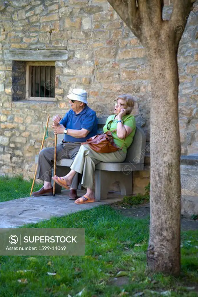 Senior citizens resting and making cell phone call on Plaza Mayor, in Ainsa, Huesca, Spain in Pyrenees Mountains, an old walled town with hilltop views of Cinca and Ara Rivers