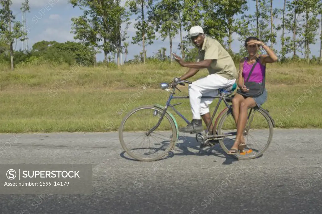 Man bicycling with woman on the back of the bike through the countryside of central Cuba