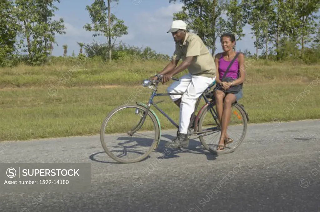 Man bicycling with woman on the back of the bike through the countryside of central Cuba