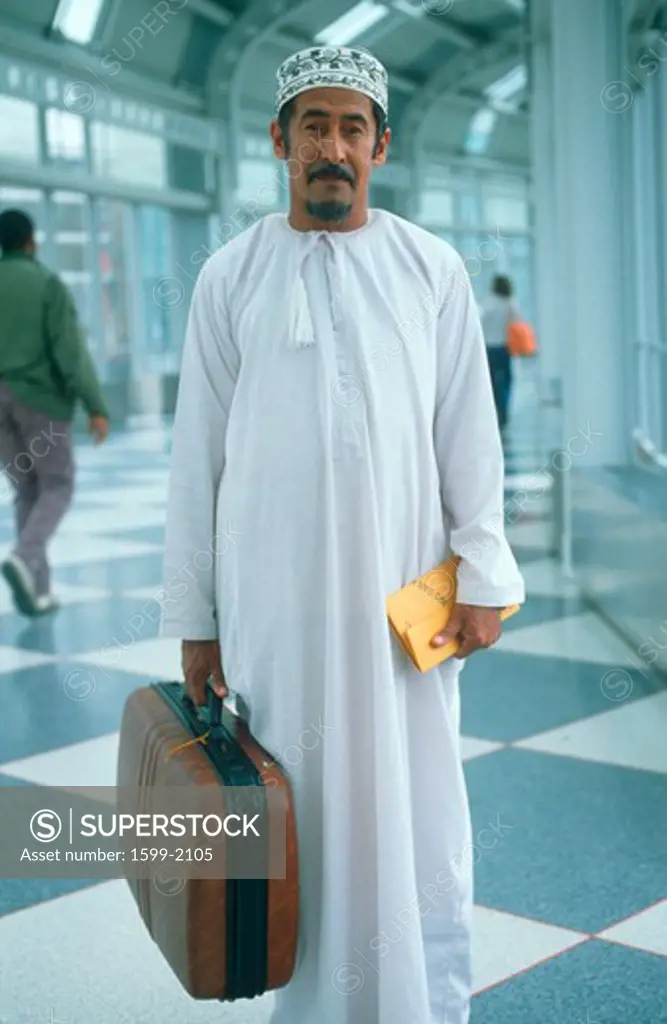 Middle Eastern man wearing white robes holding suitcase, JFK Airport, New York