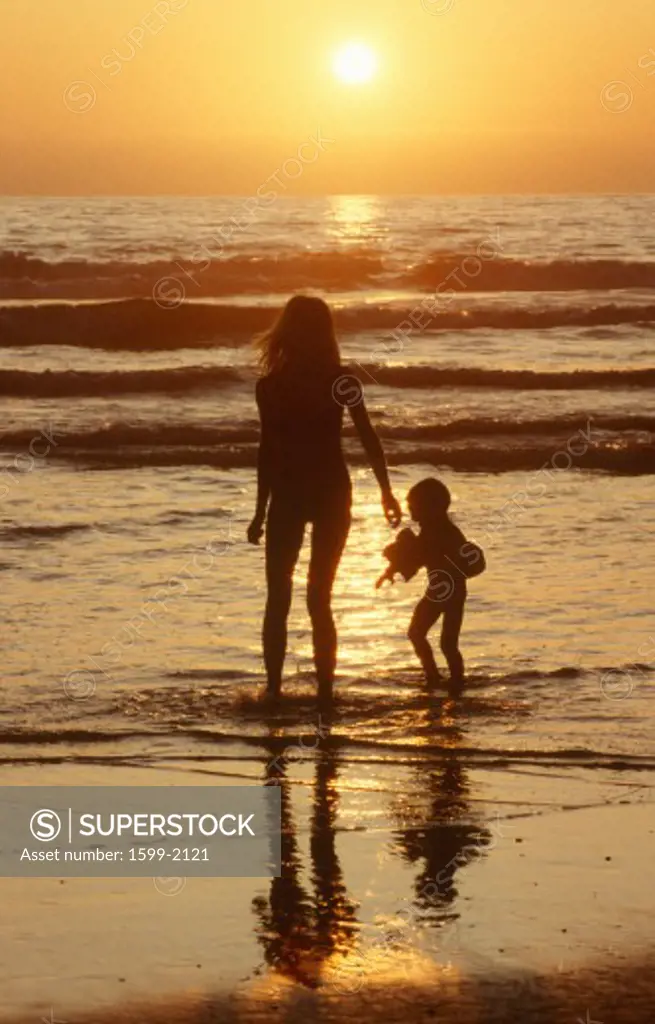 Silhouetted girl and child walking on beach at sunset, San Diego, California