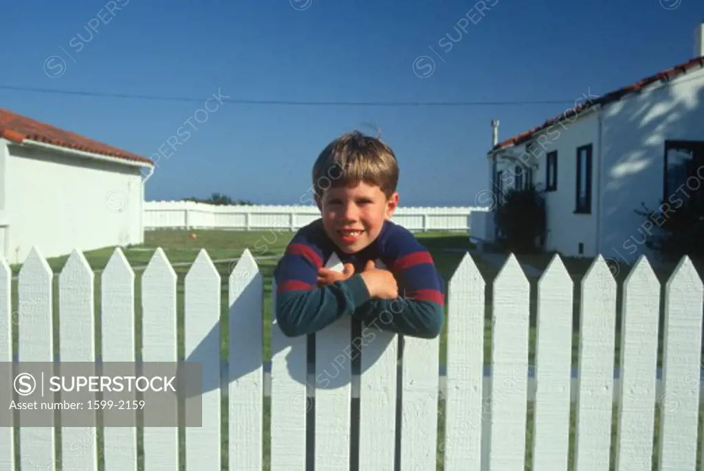Boy standing at white picket fence, Pacific Grove, California