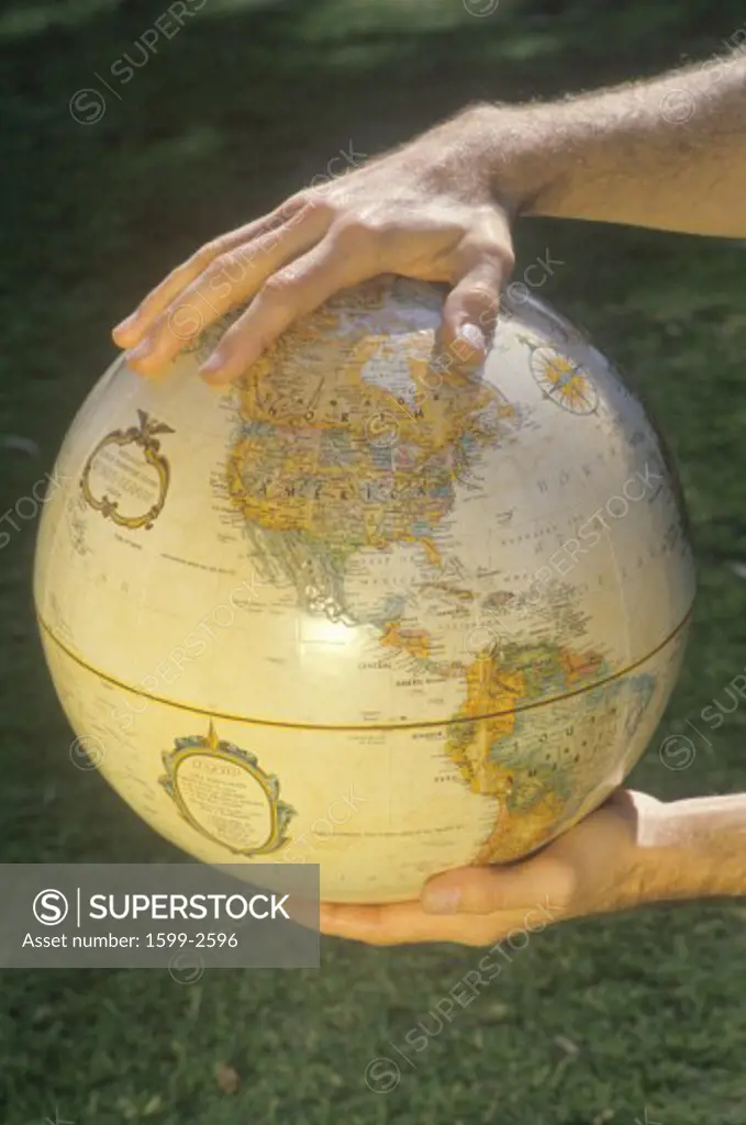 Hands holding a globe over a patch of grass 