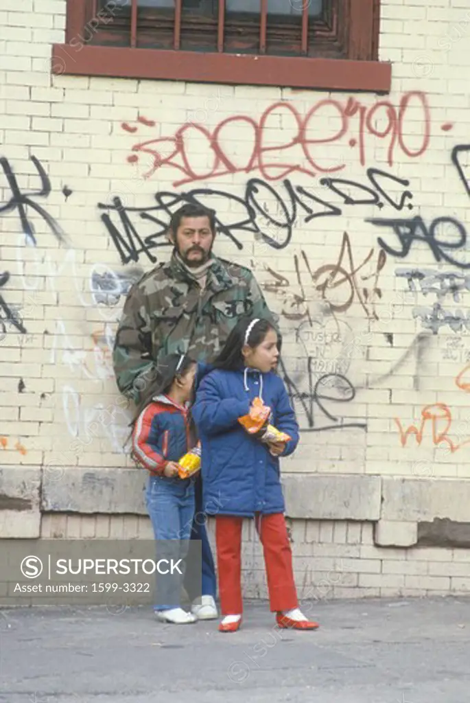 Latino man and daughters standing in front of graffiti covered walls, South Bronx, New York