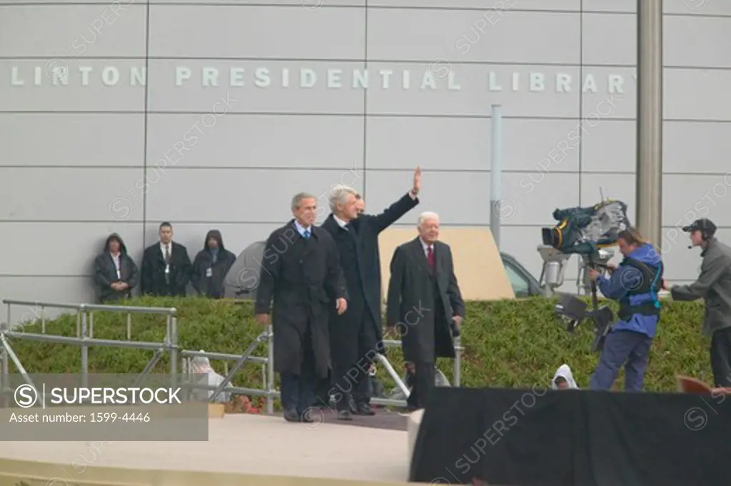 Former U.S. President Bill Clinton waves from the stage accompanied by President George W. Bush, former presidents Jimmy Carter and George H. W. Bush during the official opening ceremony of the Clinton Presidential Library November 18, 2004 in Little Rock, AK