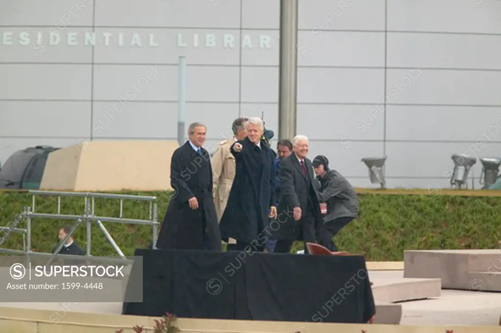 Former U.S. President Bill Clinton points from the stage accompanied by President George W. Bush, former presidents Jimmy Carter and George H. W. Bush during the official opening ceremony of the Clinton Presidential Library November 18, 2004 in Little Rock, AK