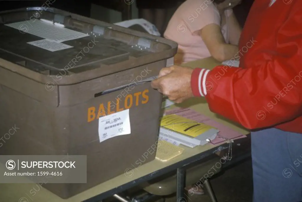 Election volunteer depositing ballots in a ballot box in a polling place, CA