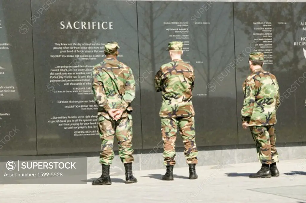 Three servicemen look at granite inscription on wall of Air Force Memorial, Arlington, Virginia in Washington D.C. area
