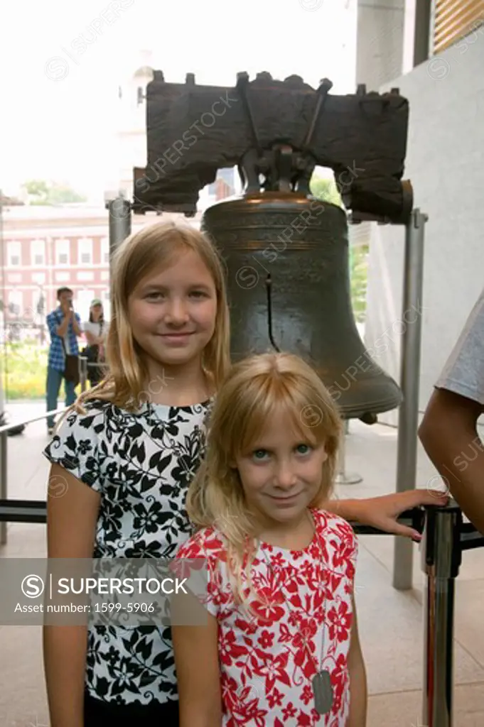 Two blond sisters stand in front of Liberty Bell, at Liberty Bell Center, in front of Independence Hall in historic area of Philadelphia, Pennsylvania