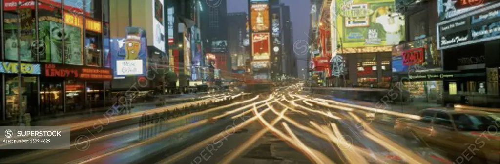 This is Times Square at night. There are streaked lights from the cars traveling through the square. There are neon lights from the billboards as well as signs.