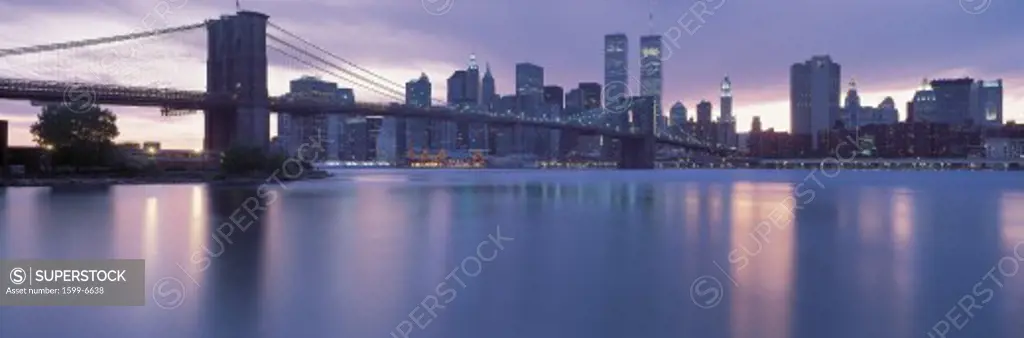 This is the Brooklyn Bridge over the East River with the Manhattan skyline at dusk. The lights of the city are starting to come on.