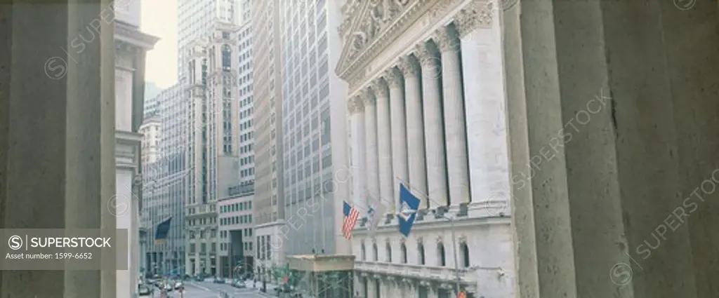 This is a view looking at the exterior of the New York Stock Exchange on Wall Street. It is framed by two white columns.