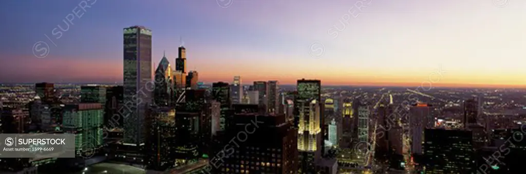 This is an aerial view of the skyline with the Sears Tower at sunset. It is a summer evening and the lights of the city are on.