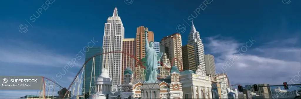This is the New York, New York Hotel and casino during the day. The buildings show a replica of the Empire State Building, the Chrysler Building, the Statue of Liberty as well as other landmark New York buildings with a large roller coaster weaving in between them.