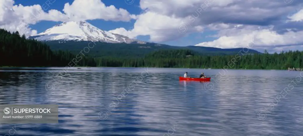 This is snow capped Mount Hood and Trillium. There is a canoeist in a red canoe on the lake .