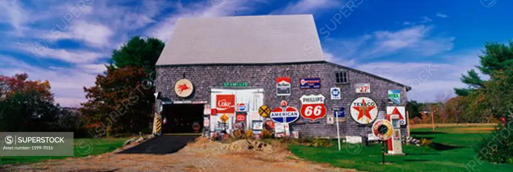 This is a New England barn with numerous signs posted on the outside of it. The signs are old advertising signs from various oil companies, as well as Marlboro. There are as a couple of vintage gas pumps from old gas stations. The owner is a collector of old signs and junk. It is a roadside attraction and piece of Americana.
