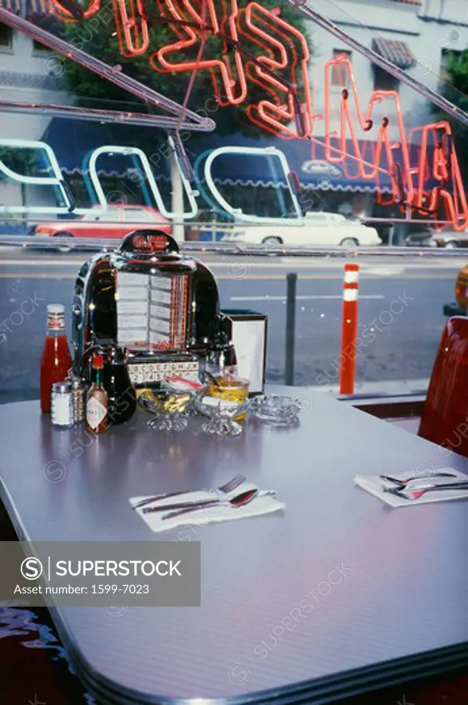 This is the interior of a vintage Americana type diner. this is one of the tables inside the diner. It has the juke box selection at the table with diner fashion salt and pepper shakers, napkin dispenser and utensils set in front of a window.
