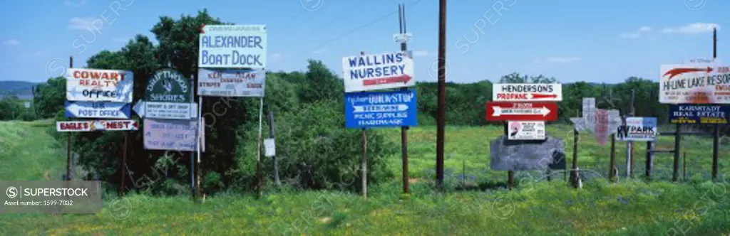 These are road signs found in the hill country in central Texas.  The signs advertise various services and point the way to find them. The time of year is spring.  There are green trees behind them and green grass below them.