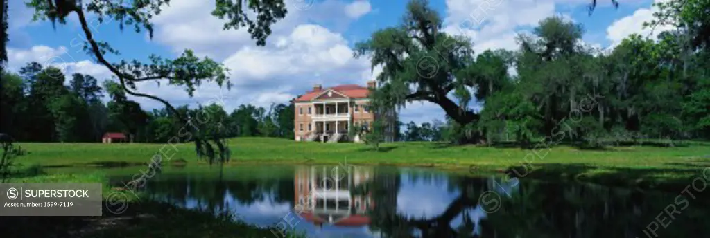 This is a southern plantation called Drayton Hall. It is a pre-Revolutionary plantation set on the Ashley River. It has Georgian Palladian architecture and was built from 1738-1742. It is set back on a green lawn with a pond showing the reflection of the plantation in the water.