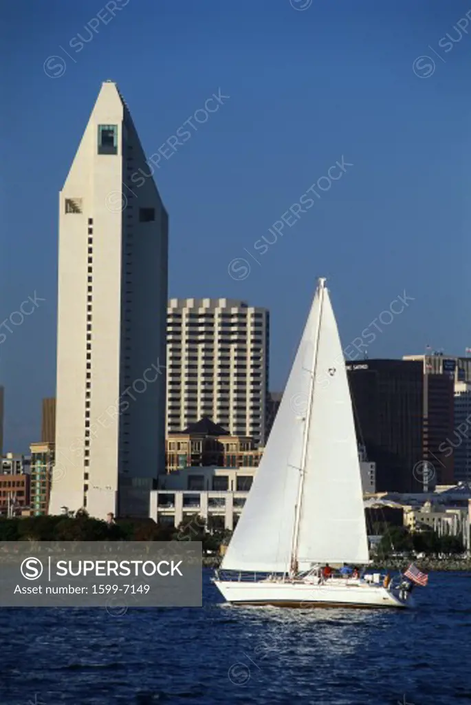 This is the San Diego Bay and skyline. It is the view from Coronado. There is a sailboat in the harbor passing in front of the skyline.