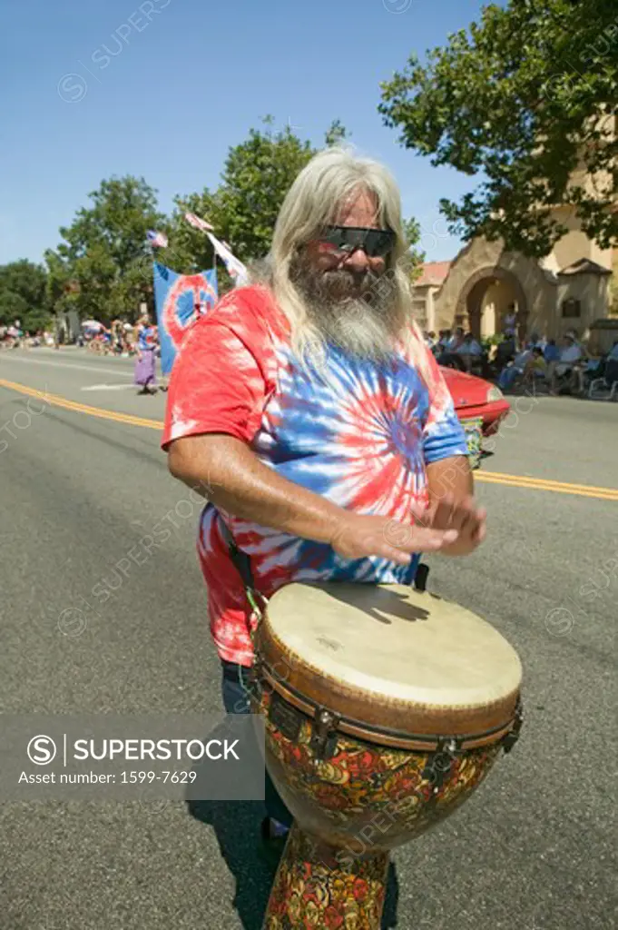 Hippie in red, white and blue tie-dye t-shirt pounds his drum down main street during a Fourth of July parade in Ojai, CA