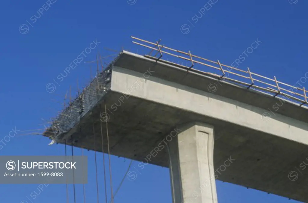 A concrete freeway structure ends abruptly with iron support structures sticking out and safety rails lining the top edge until further construction is continued, USA