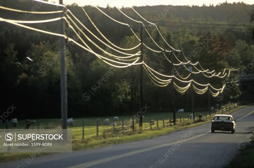 A car driving down a road with power lines during sunset in Wheelock, Vermont