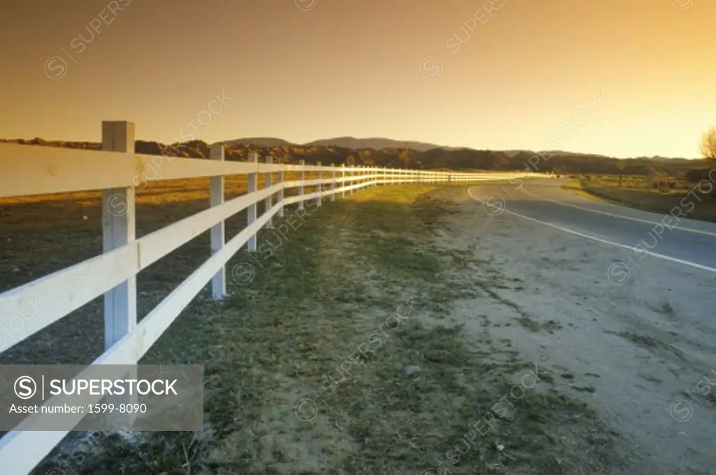 A white fence follows the path of Route 33 near Ojai into the sunset