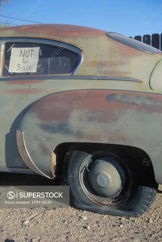 An old car with a flat tire has a not for sale sign in its window