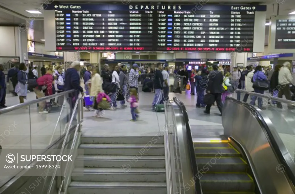 Amtrak train travelers stand in line under Departures sign, while a man goes down escalator at Penn Station, New York City, Manhattan, New York