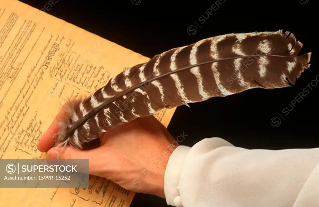 Hand holding quill pen signing U.S. Constitution