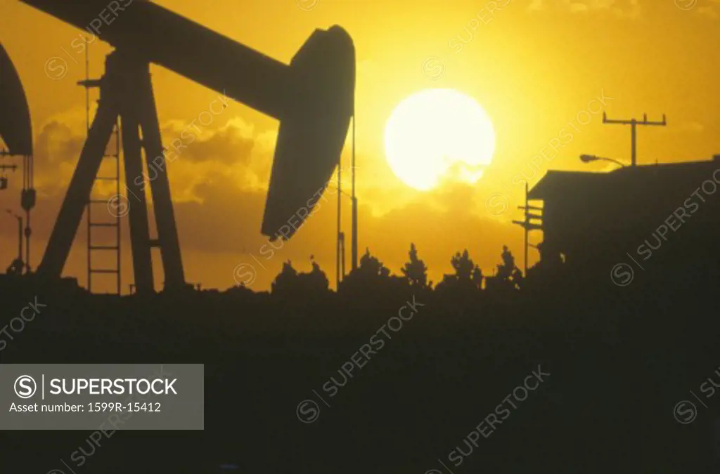Oil drilling well silhouetted at sunset