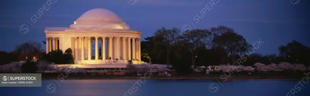This is the Jefferson Memorial next to the Tidal Basin. Cherry blossoms are blooming on the trees surrounding it at dusk.