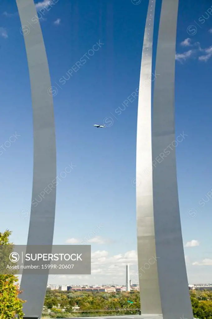 Commercial jet flies over Air Force Memorial with three soaring spires and Washington Monument in distance at One Air Force Memorial Drive, Arlington, Virginia in Washington D.C. area