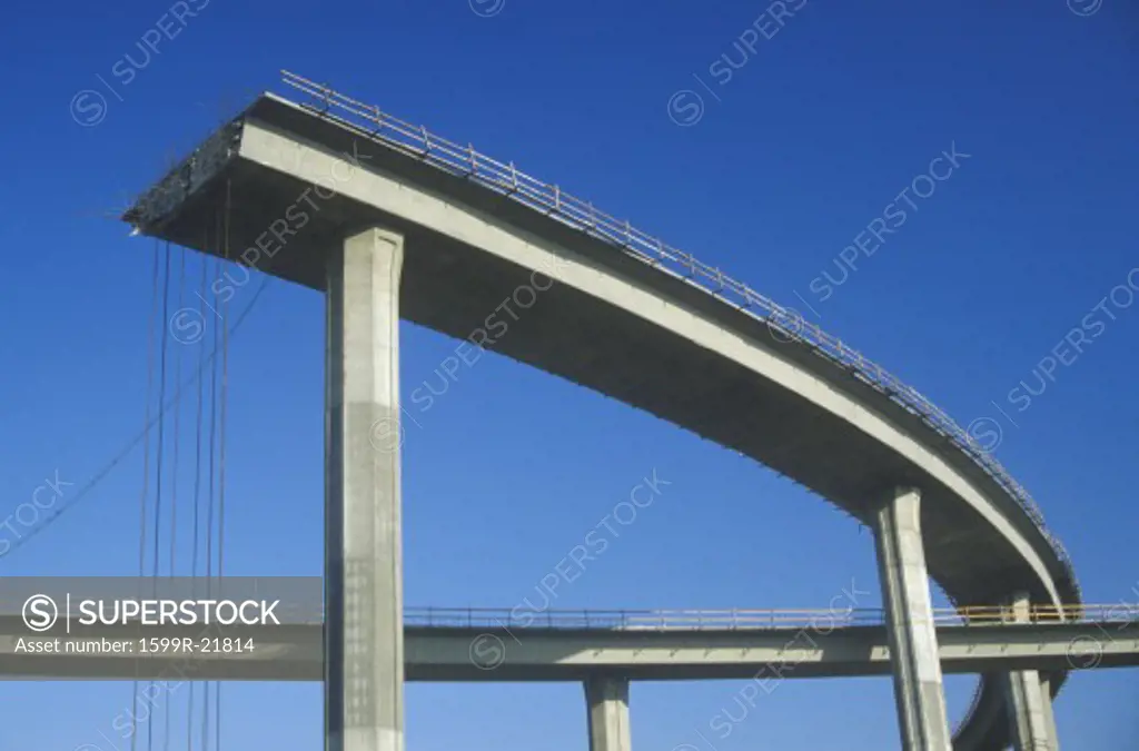 A concrete freeway structure ends abruptly with iron support structures sticking out and safety rails lining the top edge until further construction is continued, USA