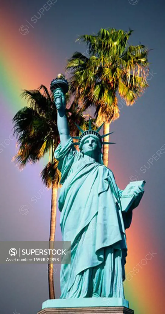 Composite image of the Statue of Liberty and pedestal against palm trees and rainbow