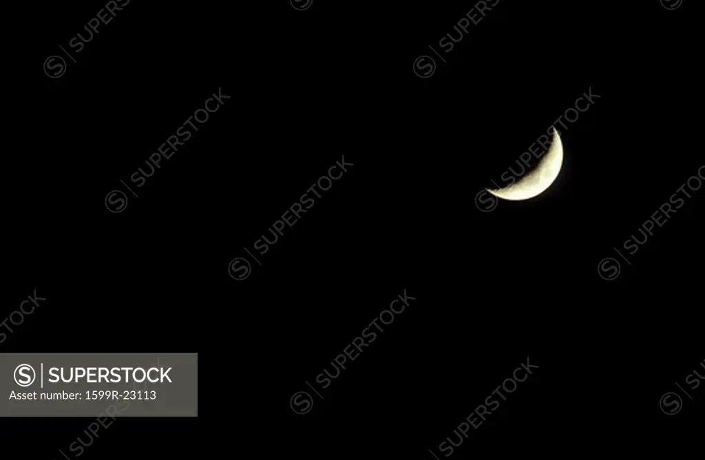 A crescent moon against a black starless sky