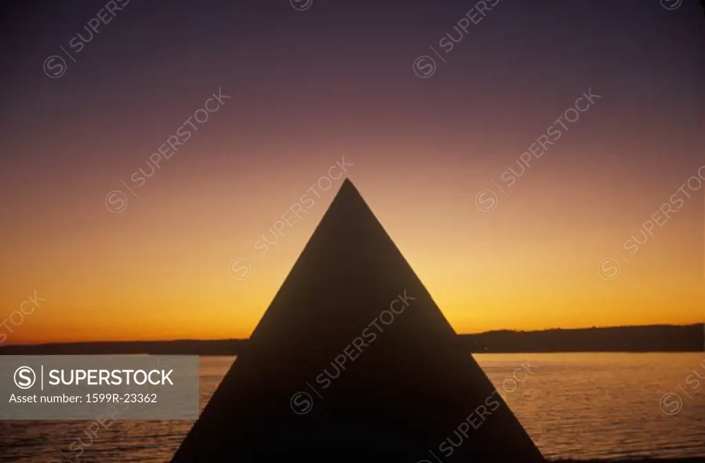 Silhouette of a pyramid by a lake and deepening orange sunset sky