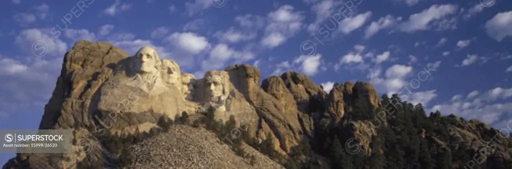 Panoramic image with white puffy clouds behind Presidents George Washington, Thomas Jefferson, Teddy Roosevelt and Abraham Lincoln at Mount Rushmore National Memorial, South Dakota
