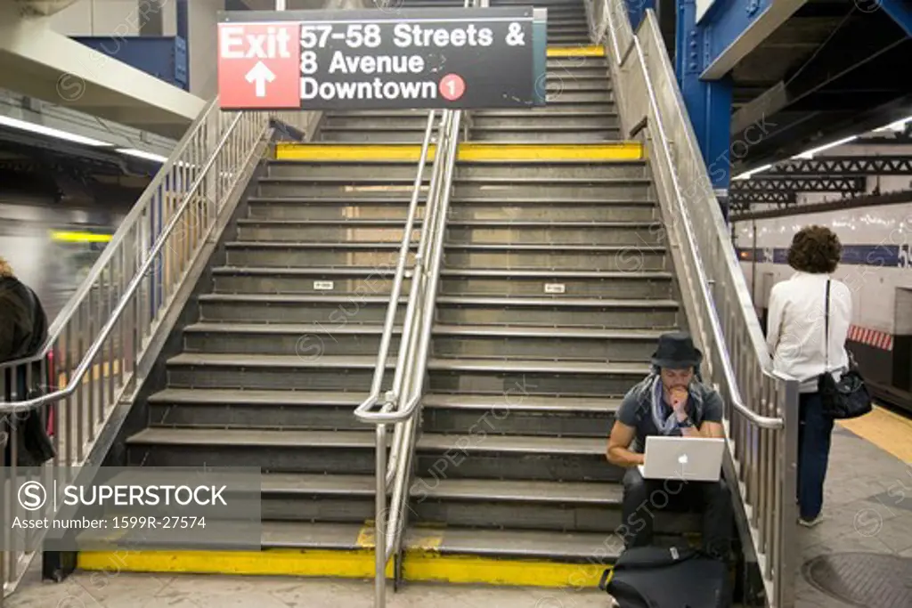 Apple laptop computer user sitting on stairwell of New York City subway system