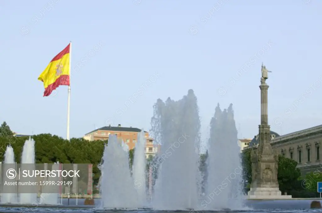 Water fountain and Spanish flag waves behind statue of Christopher Columbus at Plaza de Colón in Madrid, Spain