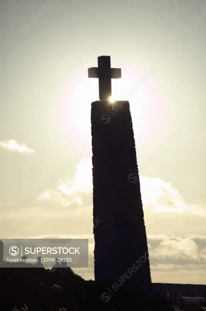 Cross with sun behind it at Cabo da Roca on the Atlantic Ocean in Sintra, Portugal, the westernmost point on the continent of Europe, which the poet Camões defined as ''where the land ends and the sea begins''.