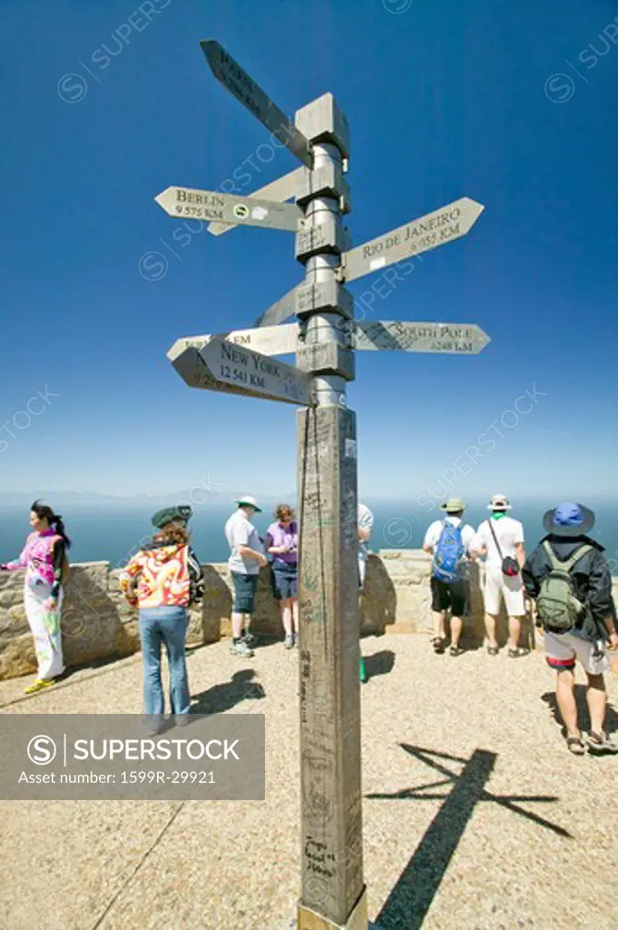 Tourists looking at view of Cape Point, Cape of Good Hope, outside Cape Town, South Africa and sign pointing to Berlin, Rio De Janeiro, New York, South Pole and other cities