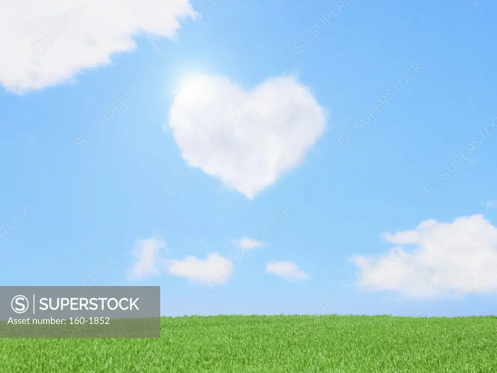 Heart-shaped cloud over green meadow, digitally generated image