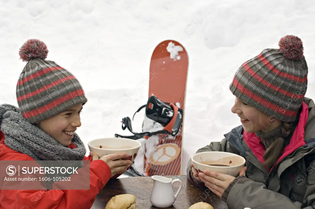 Brother and sister in ski wear eating outdoors