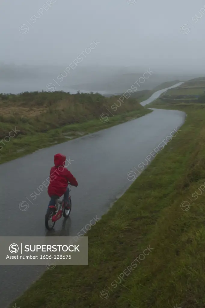 France, Brittany, Finistère, Ouessant island, child riding bike on rainy road