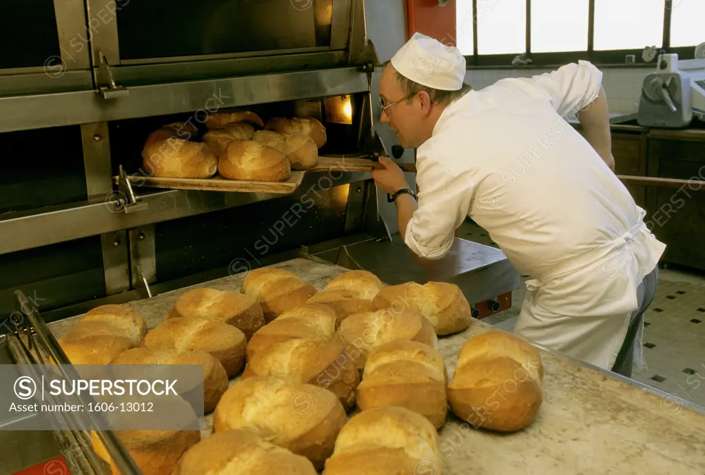 Boulanger retirant 7 miches de pain cuites du four, miches déja cuites posées sur grand plateau