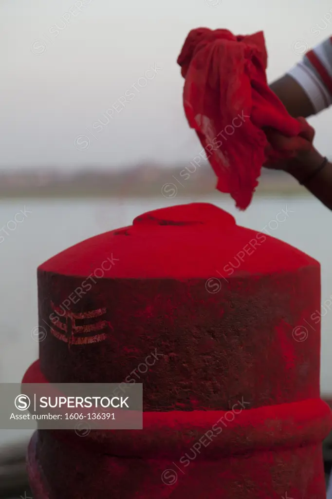 India, Utta Pradesh, Varanasi. Spreading red powder on a lingam for Holi festival. The lingam is a symbol of Shiva. India.